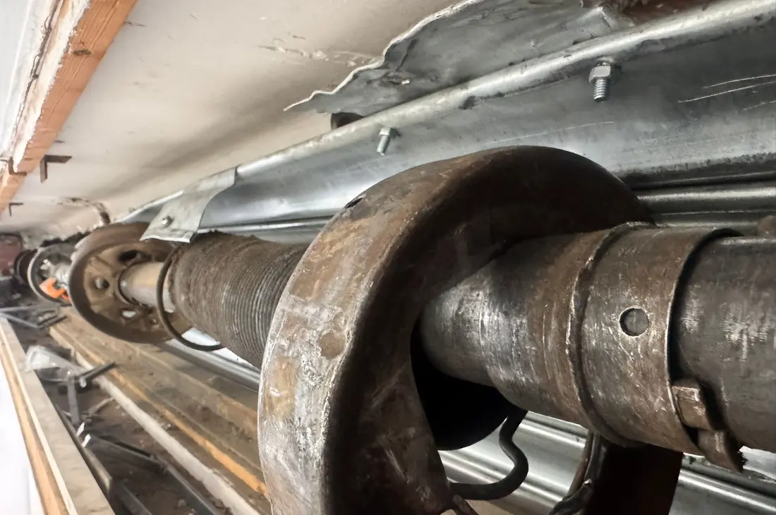 Eje de una persiana metálica con las poleas y los muelles oxidados, antes de motorizar
