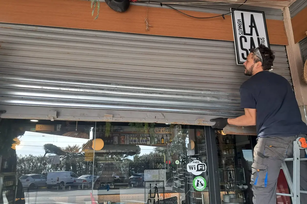 Técnico revisando la persiana metálica del cierre de un bar, subido a una escalera